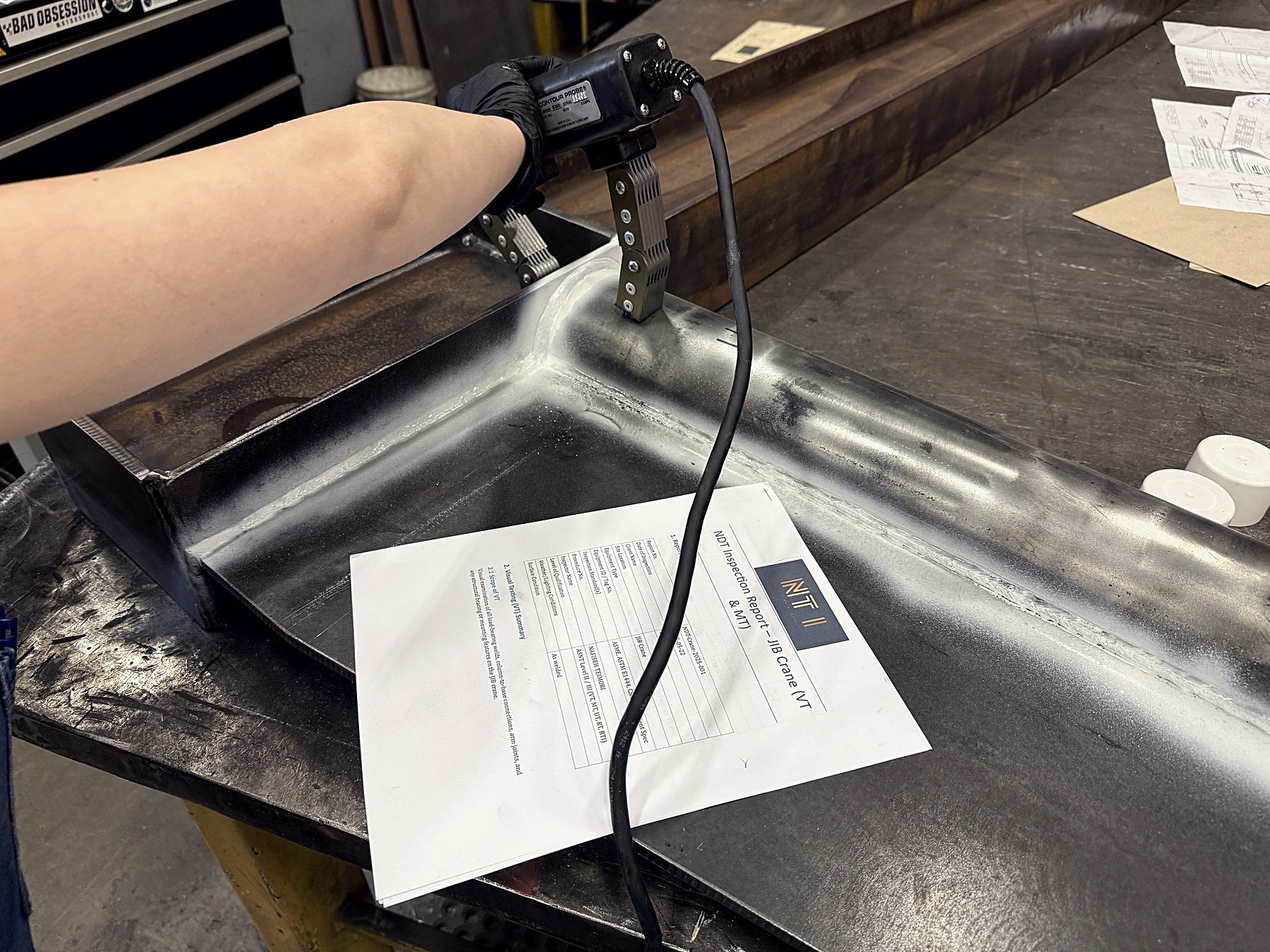 Noble Testing inspector using a contour probe next to a printed Non-Destructive Testing inspection report